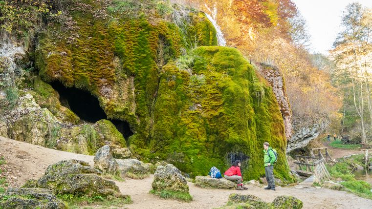Zwei Personen rasten am moosbedeckten Nohner Wasserfall in der Eifel.