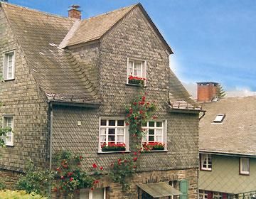 Ein charmantes, zweistöckiges Haus mit einer Holzschindelfassade. Die Fenster sind mit bunten Blumenkästen geschmückt.