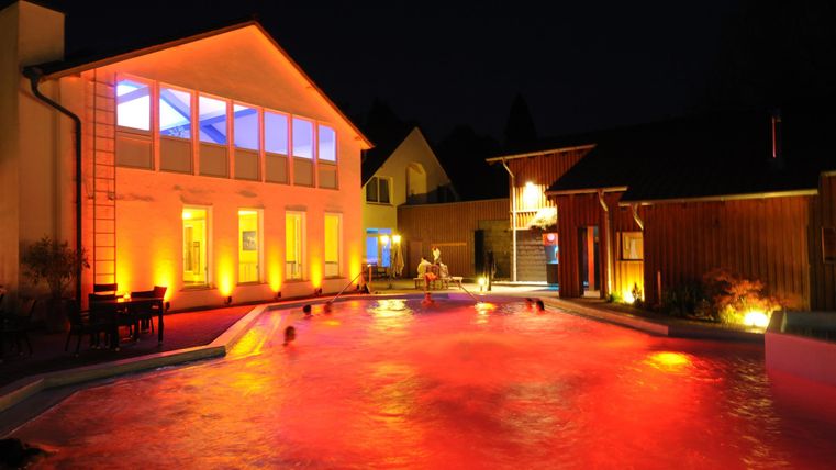 Ein wunderschöner Pool bei Nacht mit sanfter, roter Beleuchtung. Die umliegenden Gebäude sind hell erleuchtet und schaffen eine einladende Atmosphäre.