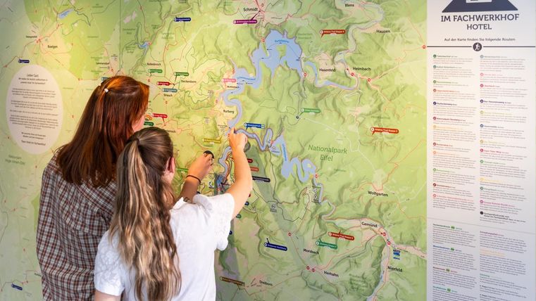 Zwei Personen betrachten eine Karte und markieren Orte. Im Hintergrund sind Informationen über die Umgebung zu sehen.