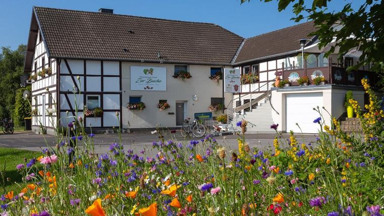 Ein charmantes Haus im Fachwerkstil mit bunten Blumen im Vordergrund. Der Himmel ist klar und die Umgebung ist einladend.