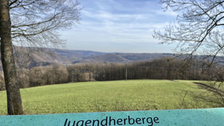 Ein schöner Blick über die Landschaft mit sanften Hügeln und Bäumen. Im Vordergrund steht das Schild einer Jugendherberge auf 470 Meter über dem Meeresspiegel.