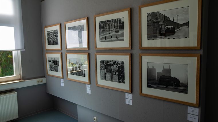 Eine Galerie mit schwarz-weiß Fotografien in gerahmten Bildern. Die Bilder zeigen verschiedene historische Szenen an einer Wand.