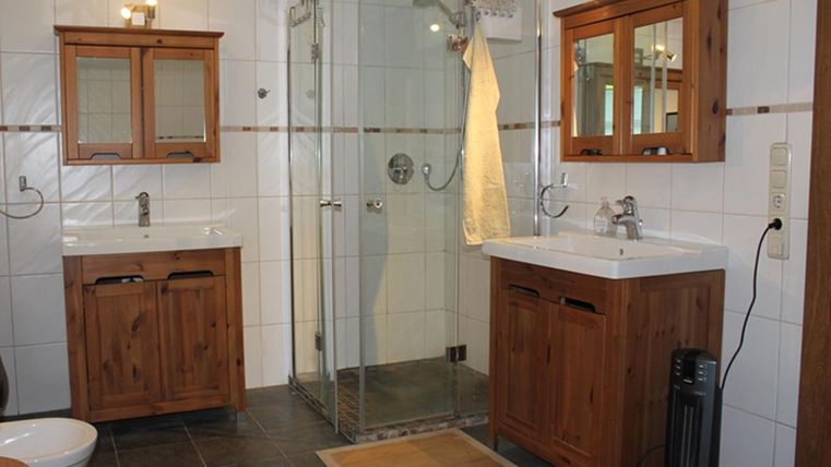 Ein modernes Badezimmer mit Holzschränken und einer Duschkabine. Der Boden ist mit dunklen Fliesen ausgelegt und ein Teppich sorgt für zusätzlichen Komfort.