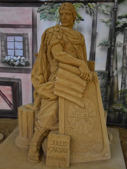 Eine beeindruckende Sandskulptur von Julius Caesar, der auf einem Podest sitzt. Der Künstler hat die Details seiner Rüstung und seines Gesichts meisterhaft dargestellt.