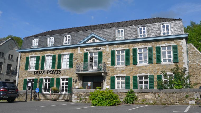 Ein charmantes Steingebäude mit grünen Fensterläden in einer ruhigen Umgebung. Das Gebäude beherbergt ein Restaurant namens "Deux Ponts".