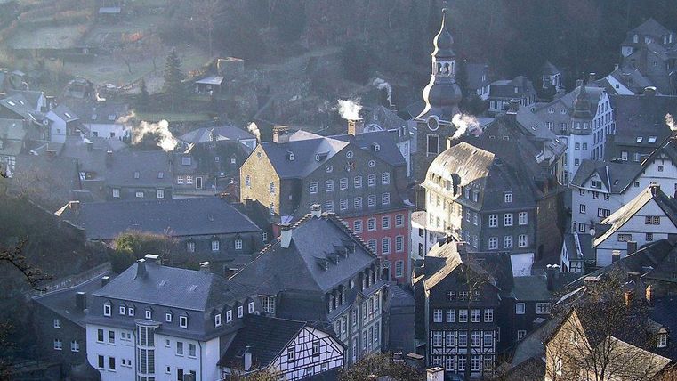 Eine malerische Stadt mit engen Gassen und historischen Häusern. Einige Gebäude haben bunte Fassaden und es steigt Rauch aus den Schornsteinen auf.