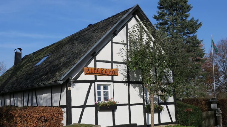 Ein traditionelles Fachwerkhaus mit einem sichtbaren Schild. Der Himmel ist klar und blau, umgeben von Bäumen und Sträuchern.
