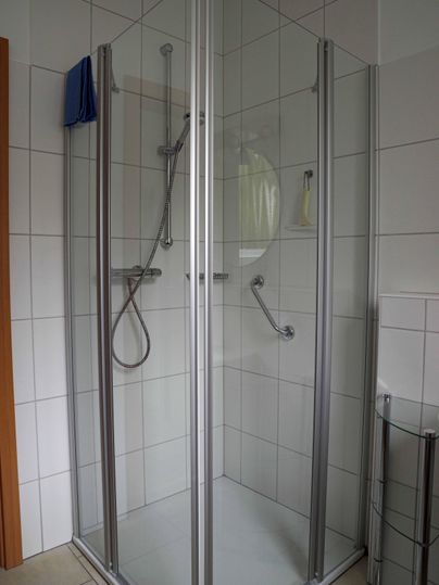 Eine moderne Dusche mit glasklaren Wänden und silbernen Rahmen. Die Wände sind gefliest und die Ausstattung ist funktional.