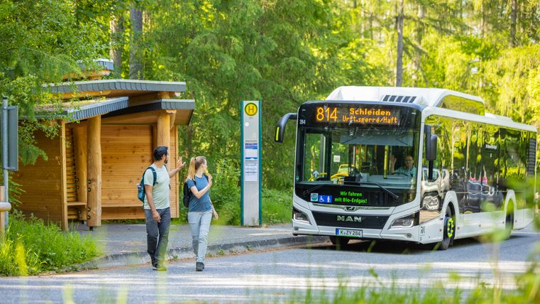 Ein Mann und eine Frau winken dem Busfahrer in einem Bus vor der Haltestelle zu