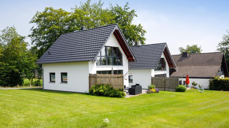 Zwei moderne Häuser mit Satteldächern stehen in einer grünen Umgebung. Der Garten ist gepflegt und bietet einen einladenden Außenbereich.