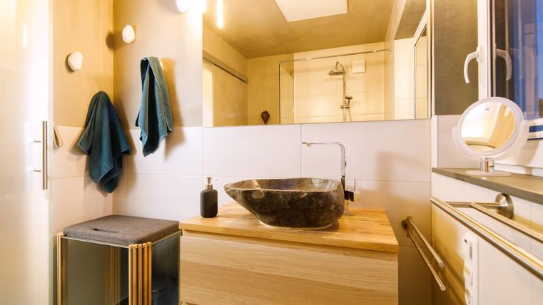 Ein modernes Badezimmer mit Holzdetails und einer eleganten Waschschüssel. An der Wand hängen Handtücher, und es gibt eine große Fensterfläche für viel Licht.