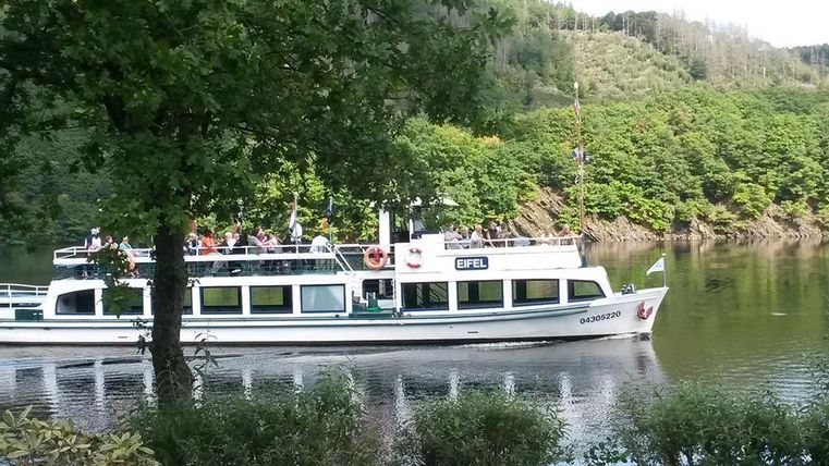 Ein Ausflugsboot fährt auf einem ruhigen Fluss, umgeben von grünen Hügeln. Die Landschaft ist idyllisch und lädt zur Entspannung ein.