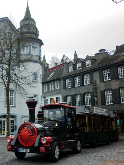 Eine kleine Touristenbahn steht auf einem gepflasterten Platz. Im Hintergrund sind historische Gebäude zu sehen.