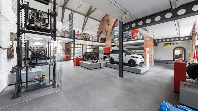 Ein modernes Ausstellungsgebäude mit verschiedenen Fahrzeugen und Maschinen. Der Raum ist hell und offen, mit einem industriellen Stil.