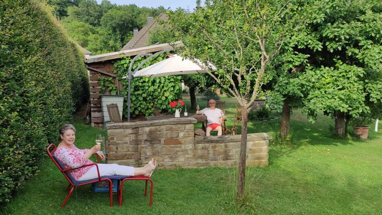 Ein einladender Garten mit zwei Personen, die entspannt sitzen. Im Hintergrund sind Bäume und ein Pavillon zu sehen.