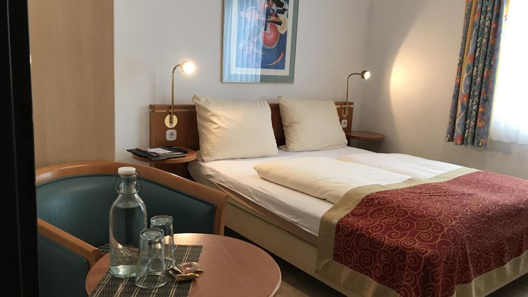 Ein gemütliches Hotelzimmer mit einem Doppelbett und einem kleinen Tisch. Auf dem Tisch stehen Wasserflaschen und Gläser.