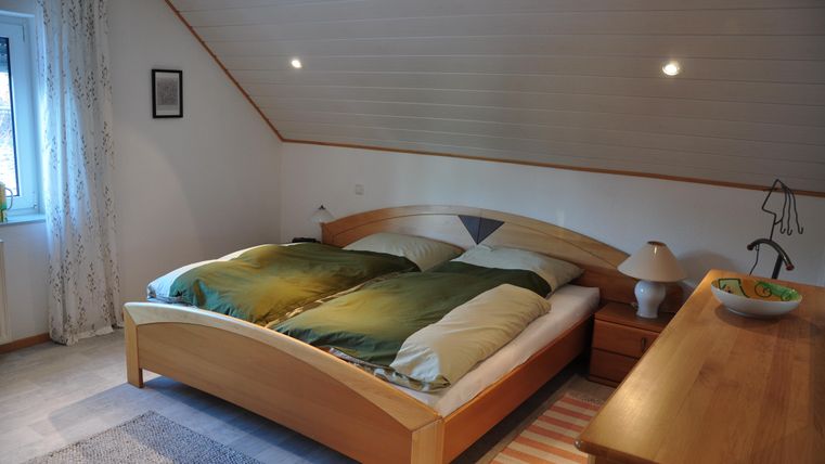 Ein gemütliches Schlafzimmer mit einem großen Doppelbett und Holz-Möbeln. Warme Farben und sanftes Licht schaffen eine einladende Atmosphäre.