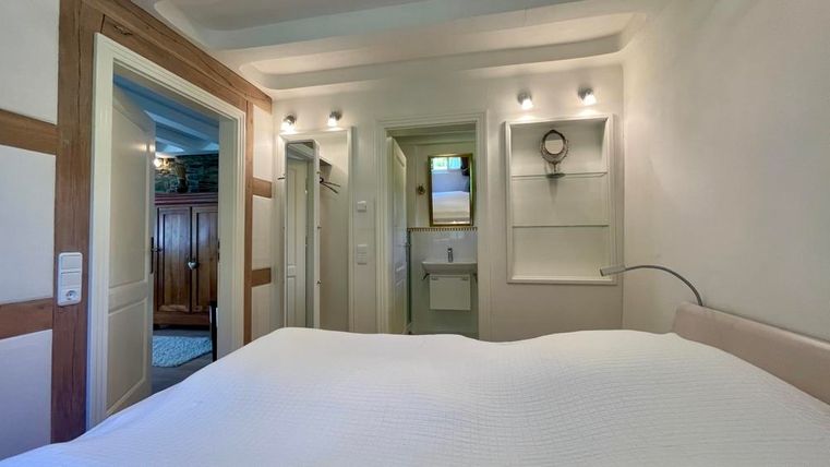 Ein helles Schlafzimmer mit einem großen Bett und einfachen, modernen Möbeln. Die Wände sind in neutralen Farbtönen gehalten und es gibt einen Blick auf einen kleinen Flur.