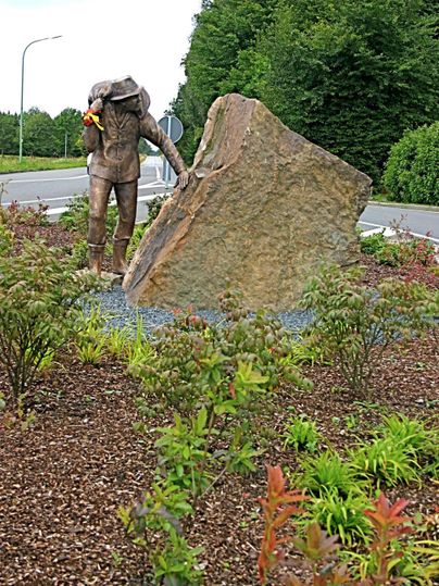Eine Statue eines Tauchers, der mit einem großen Stein interagiert. Umgeben von bunten Pflanzenanlagen.