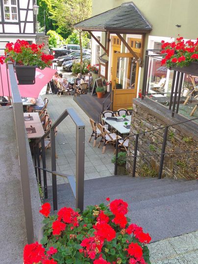 Ein charmantes Restaurant mit blühenden roten Geranien und gemütlichen Tischen im Freien. Die Umgebung ist grün und einladend, ideal für entspannte Stunden.