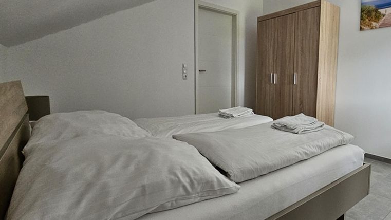 Ein komfortables Schlafzimmer mit einem Doppelbett und frischen Handtüchern. Im Hintergrund steht ein Holzschrank neben einer Tür.