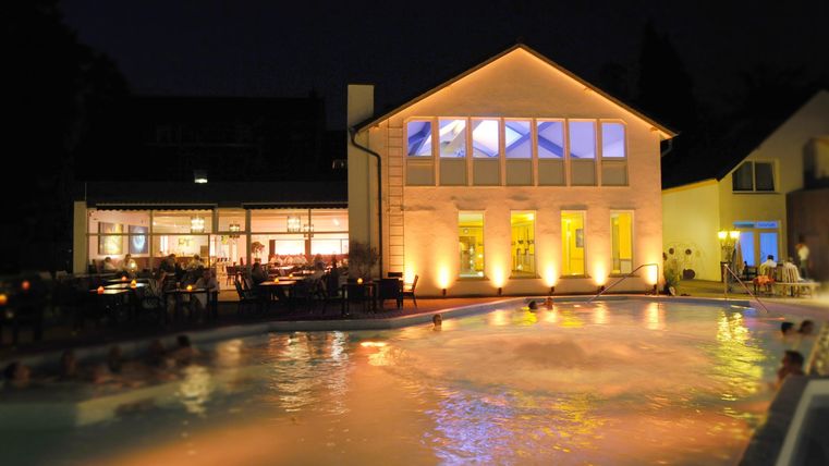 Ein schöner Pool bei Nacht, umgeben von beleuchteten Gebäuden. Sanfte Lichter reflektieren sich auf dem Wasser.