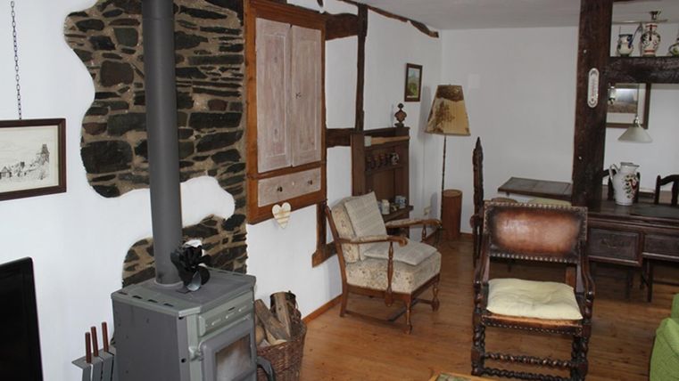 Ein gemütlicher Wohnraum mit einem Holzofen und rustikalen Möbeln. Die Wände sind teilweise mit Stein und Holz verkleidet.