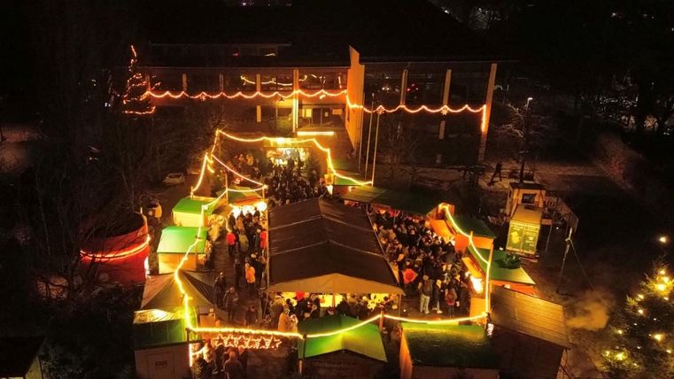 Eine festlich beleuchtete Veranstaltung im Freien mit zahlreichen Menschen. Bunte Lichter und Stände schaffen eine einladende Atmosphäre.