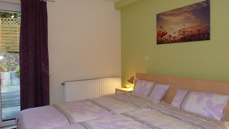 Ein gemütliches Schlafzimmer mit zwei Betten und lila Bettwäsche. An der Wand hängt ein Bild mit einer Blumenlandschaft, und ein Fenster mit Blick ins Freie ist vorhanden.