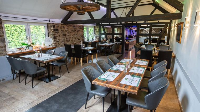 Ein modernes Restaurant mit Holzbalken und eleganten Tischen. Die Einrichtung ist hell und einladend, mit großen Fenstern, die viel Licht hereinlassen.