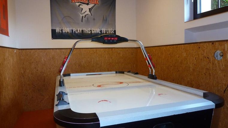 Ein Airhockey-Tisch steht in einem Raum mit Holzvertäfelung. An der Wand hängt ein Banner mit dem Schriftzug "WE DON'T PLAY THIS GAME TO LOSE".