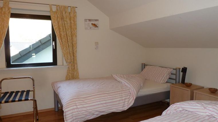 Ein schlichtes Schlafzimmer mit zwei Einzelbetten und Holzfußboden. Das Fenster lässt natürliches Licht herein und es gibt einen Stuhl aus Metall.