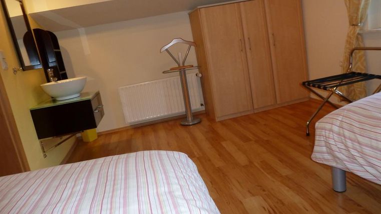 Ein schlichtes Zimmer mit zwei Betten und Holzfußboden. Im Vordergrund sind ein Waschbecken und ein Kleiderschrank zu sehen.