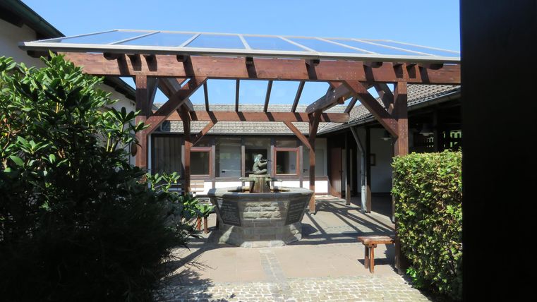 Ein schöner Innenhof mit einem Holzpergola und einer Solaranlage. Im Hintergrund ist ein Brunnen und gepflegte Pflanzen zu sehen.