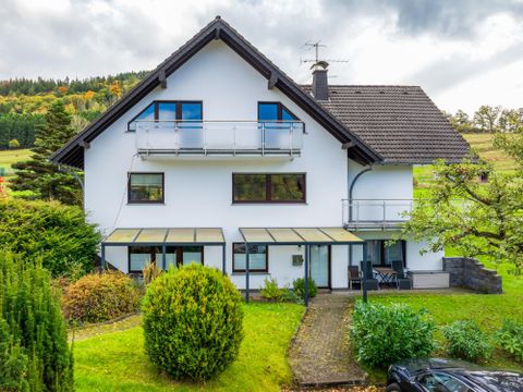 Ein modernes Haus mit einem großen Garten. Es hat Balkone und ist von Bäumen umgeben.