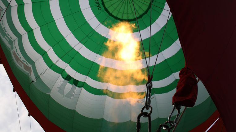 Ein Blick ins Innere eines Heißluftballons mit grünen und weißen Streifen. Flammen entfalten sich unter dem Ballon und erzeugen Wärme.