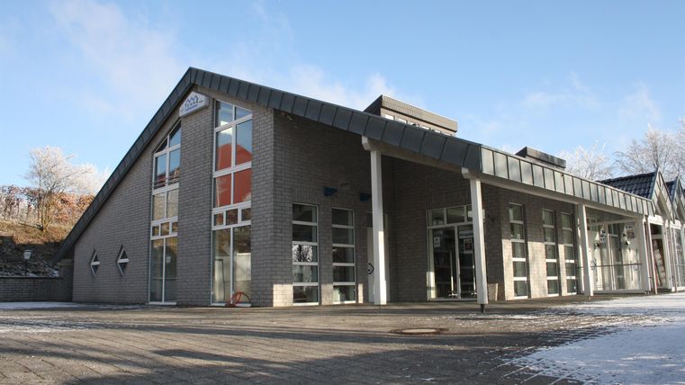 Ein modernes Gebäude mit großen Fenstern und einem schrägen Dach. Der Himmel ist klar und es gibt Schnee auf dem Boden.