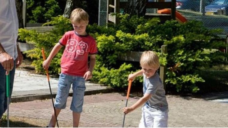 Ein Spielplatz mit Kindern, die mit Stöcken spielen. Es ist ein sonniger Tag und die Kinder haben viel Spaß.